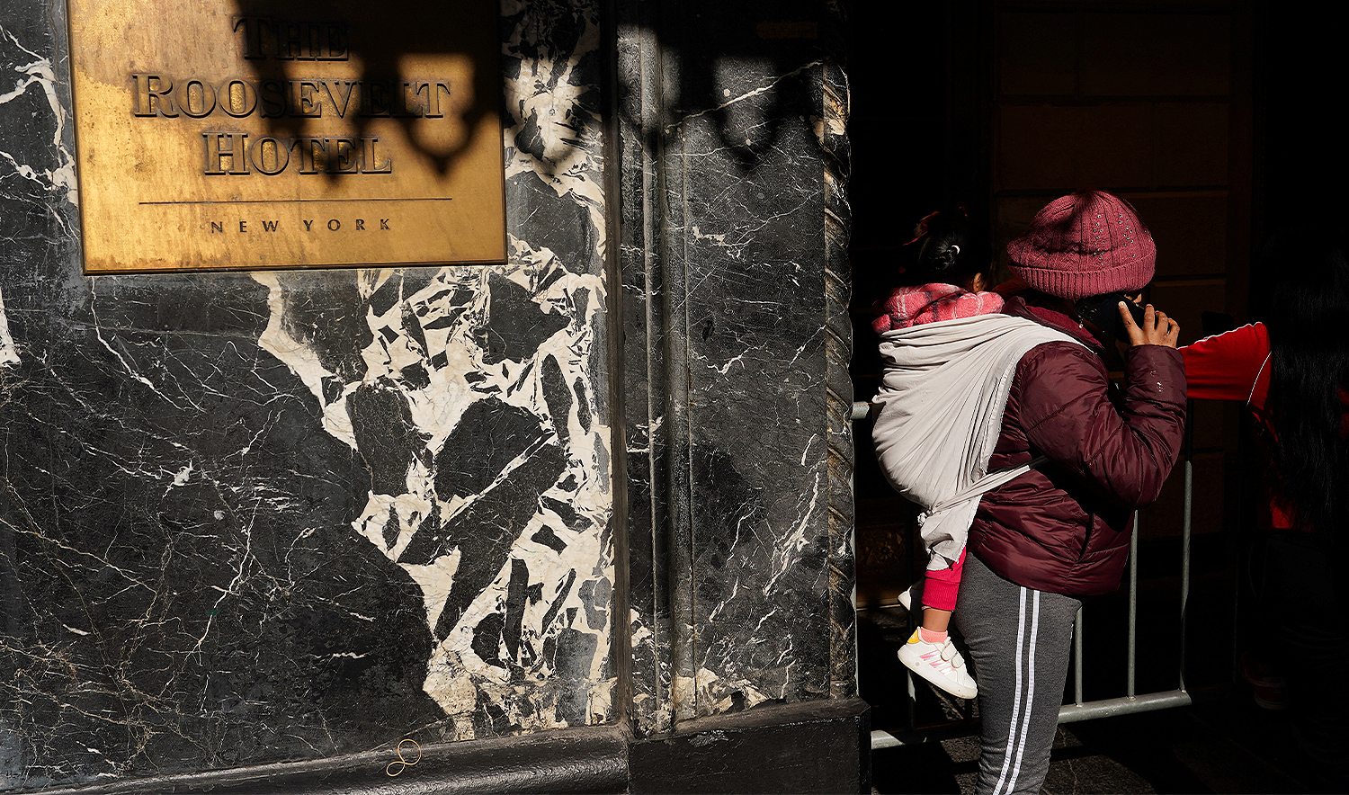 A migrant carrying a child speaks on the phone outside of The Roosevelt Hotel after New York City Mayor Eric Adams announced the forthcoming closure of the Asylum Seeker Arrival Center and Humanitarian Emergency Response and Relief Center located at The Roosevelt Hotel, in midtown Manhattan in New York City, US, on February 24, 2025. (REUTERS/File)