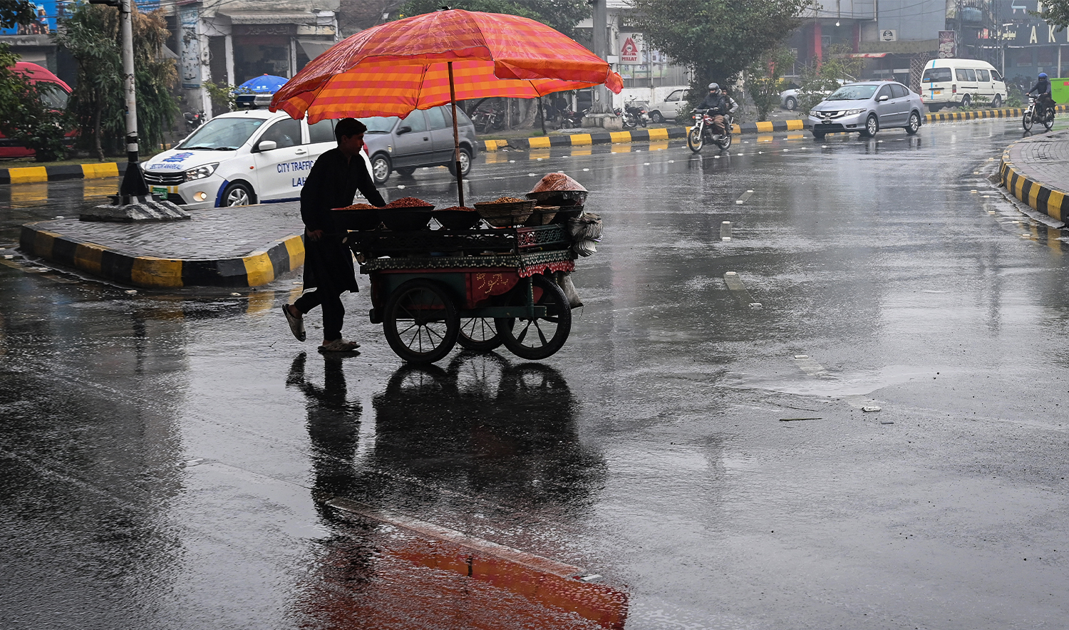 A vendor pushes his food cart as he walks across a road during rainfall in Lahore on December 27, 2024. (AFP/File)