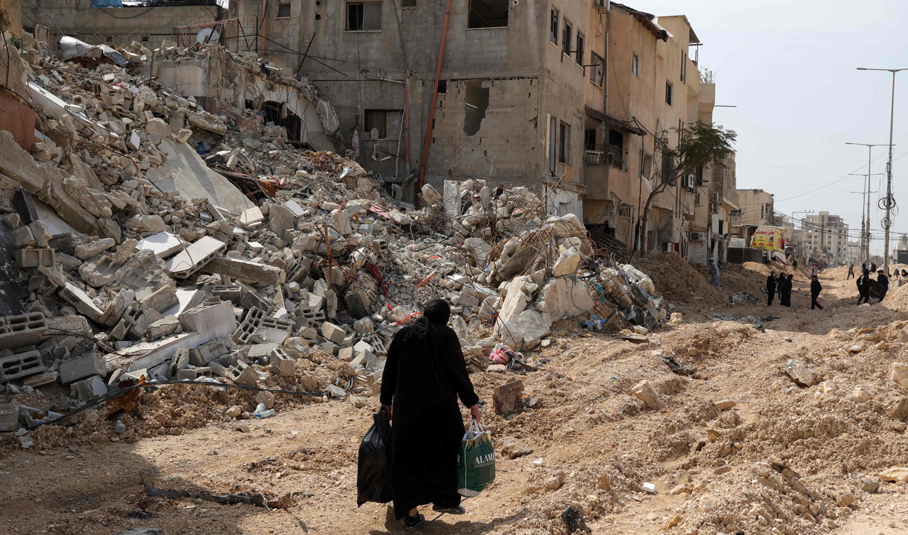 A woman carrying some personal items walks along a devastated street as she leaves the Nur Shams camp for Palestinian refugees, where Israeli forces allowed residents to retrieve belongings after issuing reported demolition notifications for several houses, in the occupied West Bank on March 5, 2025. (AFP)