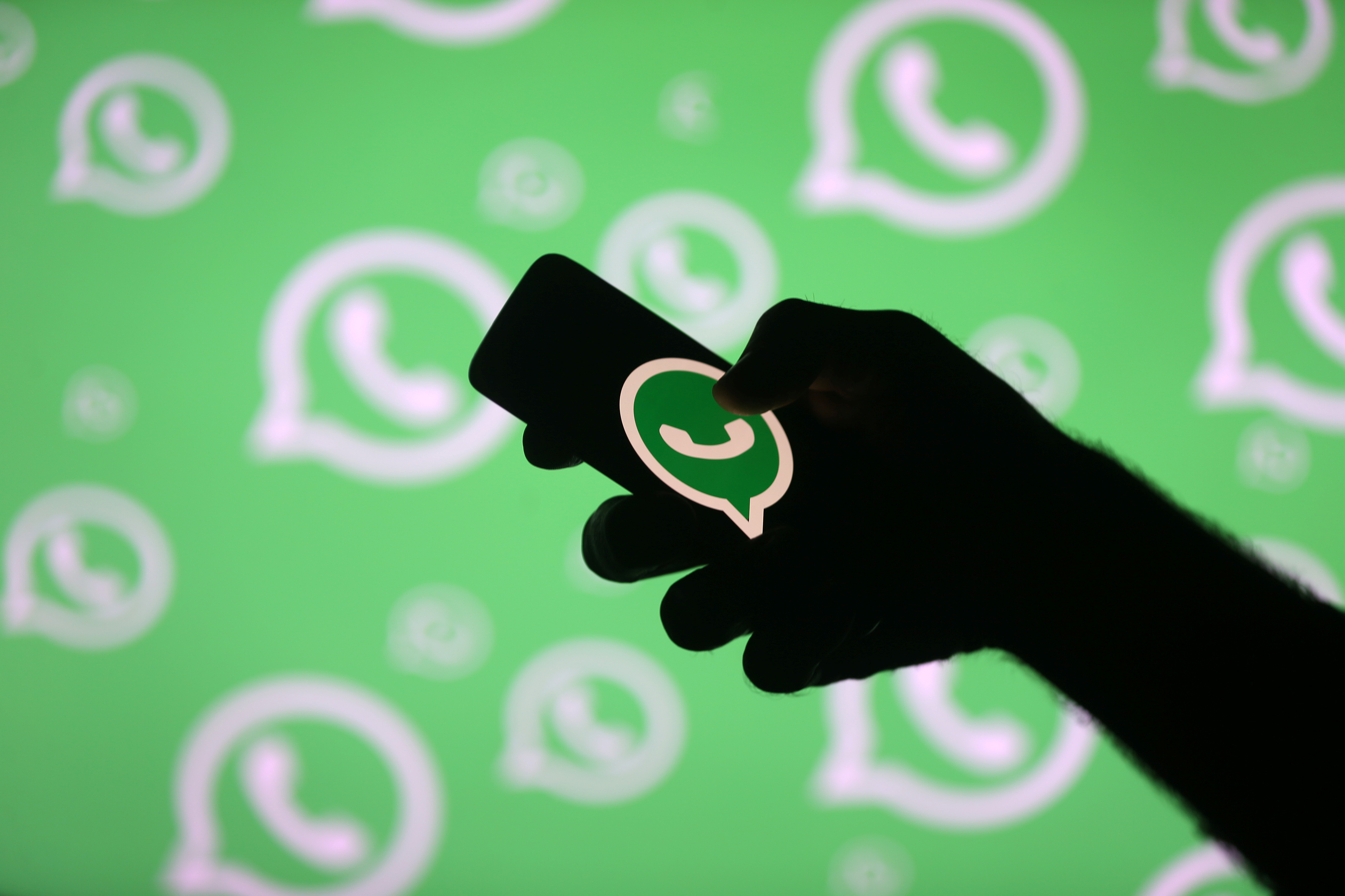 This illustration created on September 14, 2017, shows a man poses with a smartphone in front of displayed Whatsapp logo. (REUTERS/File)