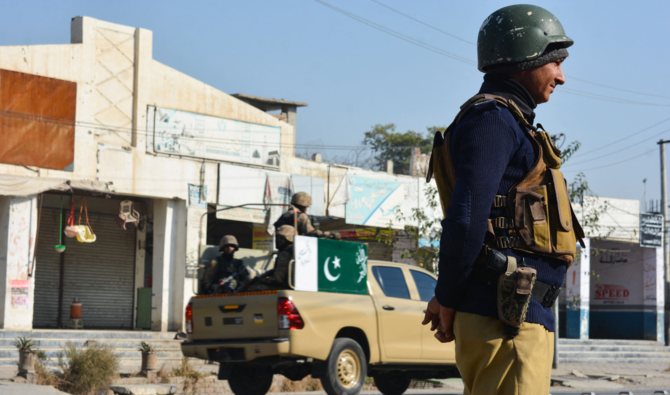 A policeman (R) and army soldiers (L) stand guard along a road in Bannu on December 21, 2022, a day after the seize of a Pakistan police station ended. (AFP/file)