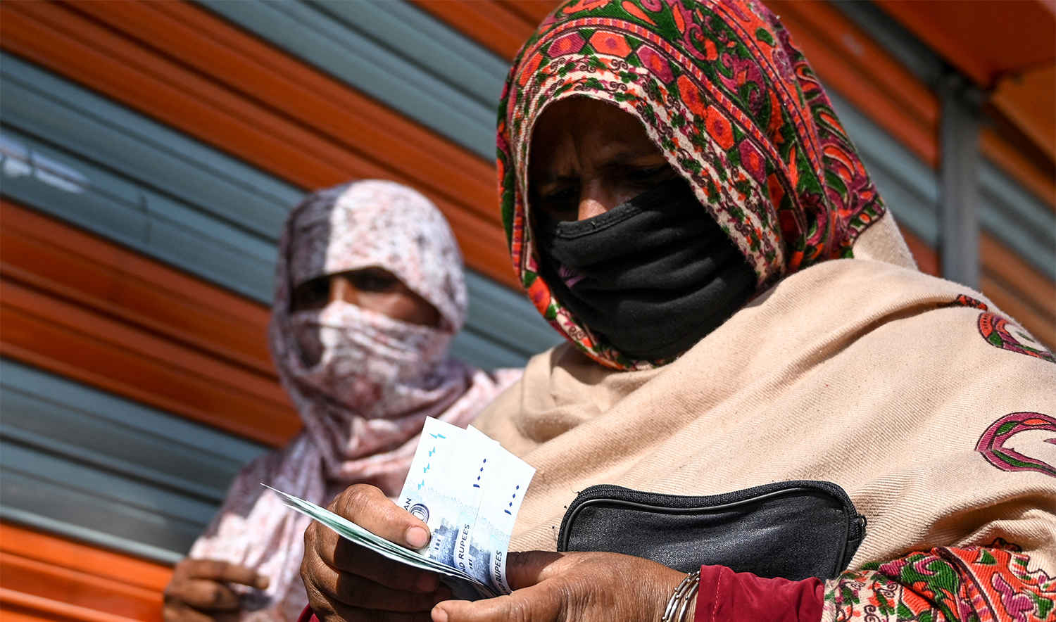 A woman (R) counts rupee notes after collecting cash of financial assistance through a mobile wallet in Islamabad on April 9, 2020. (AFP/File)
