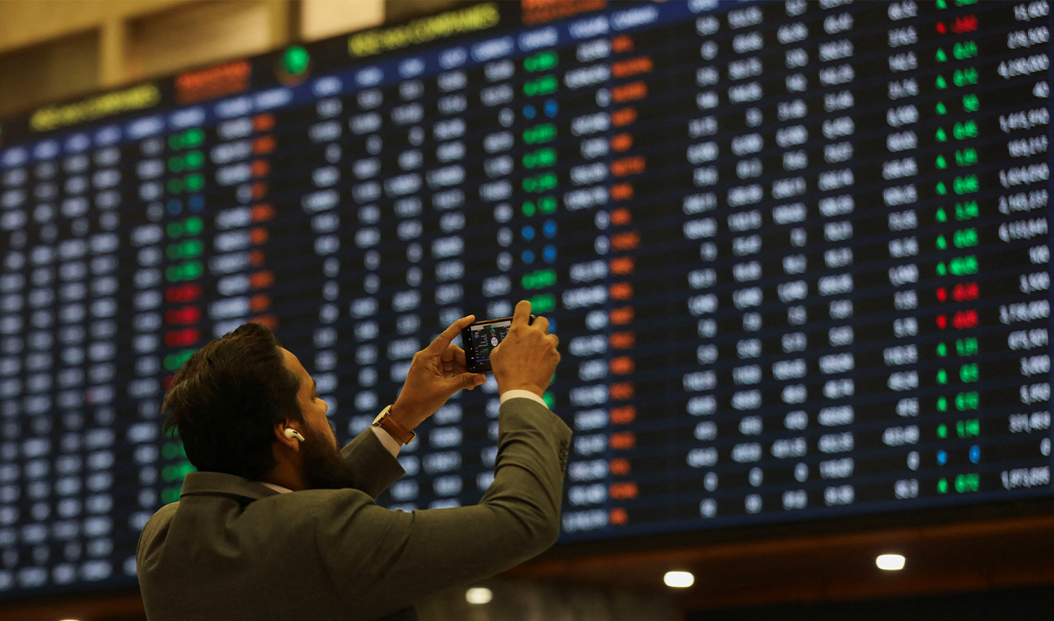 A man uses a mobile phone as he takes a photo of the electronic board displaying share prices during a trading session at the Pakistan Stock Exchange, in Karachi, Pakistan on November 28, 2023. (REUTERS/File)