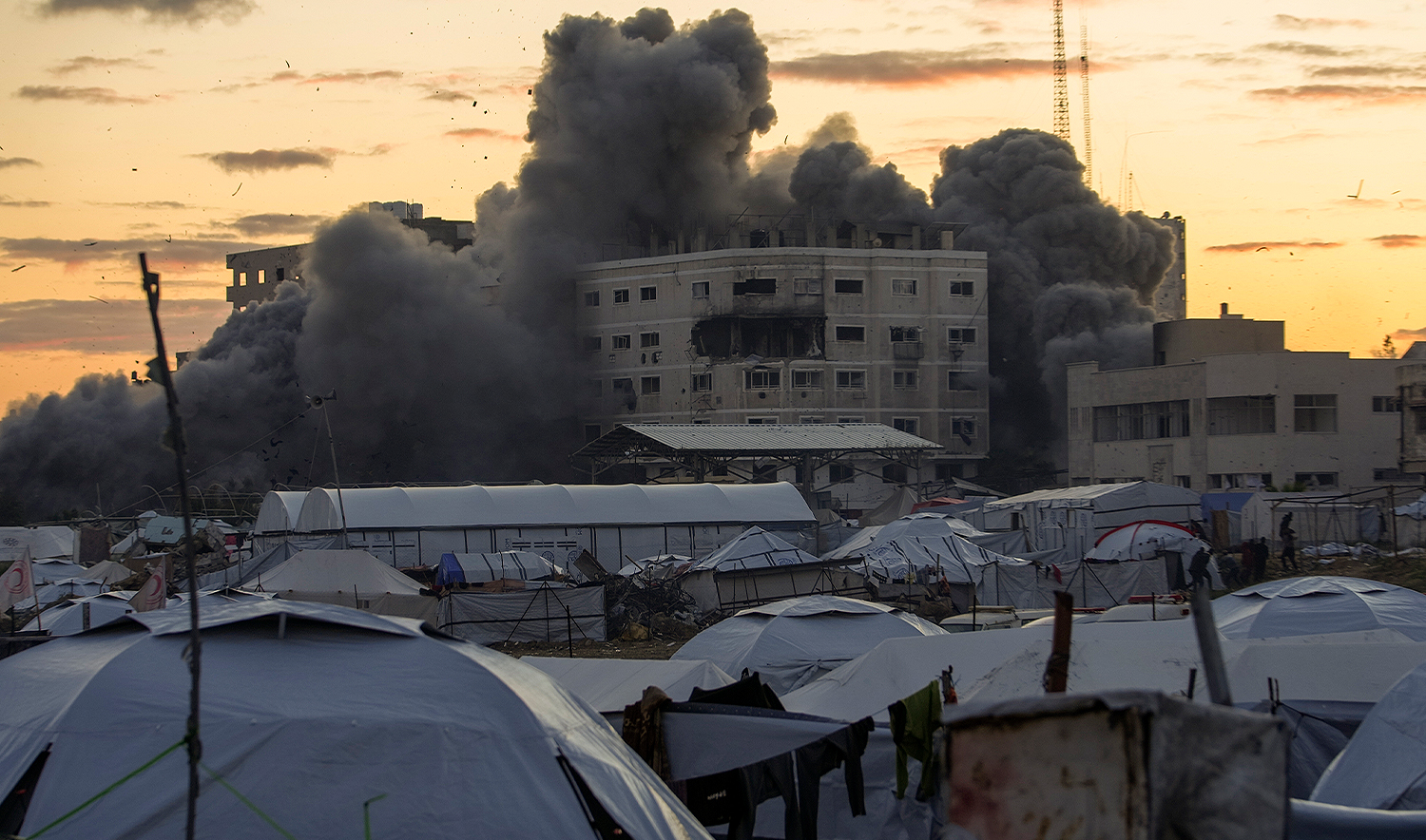Behind a tent camp for displaced Palestinians, smoke rises from a building after it was targeted by an Israeli army strike, following evacuation orders for residents in Gaza City on March 22, 2025. (AP)