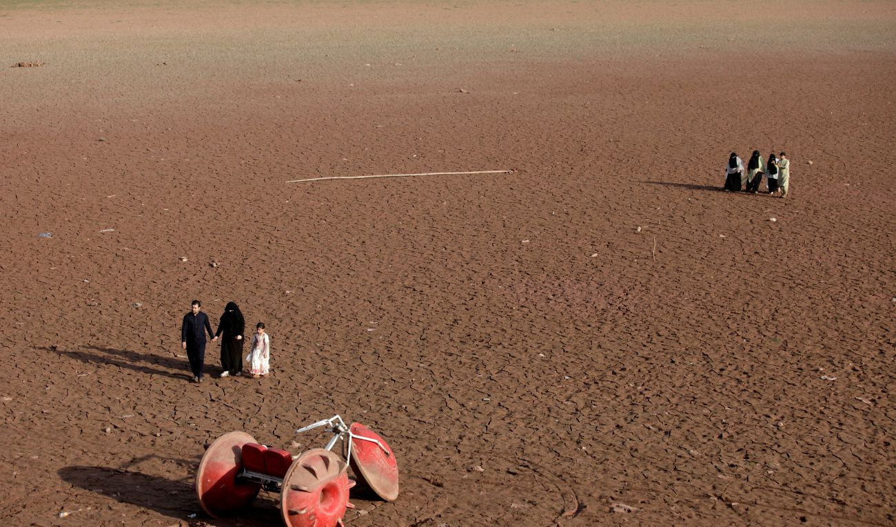 People walk near a three-wheeler parked at a dry portion of land that used to have water, at the bank of Rawal lake in Islamabad, Pakistan June 20, 2018. (REUTERS/ file)