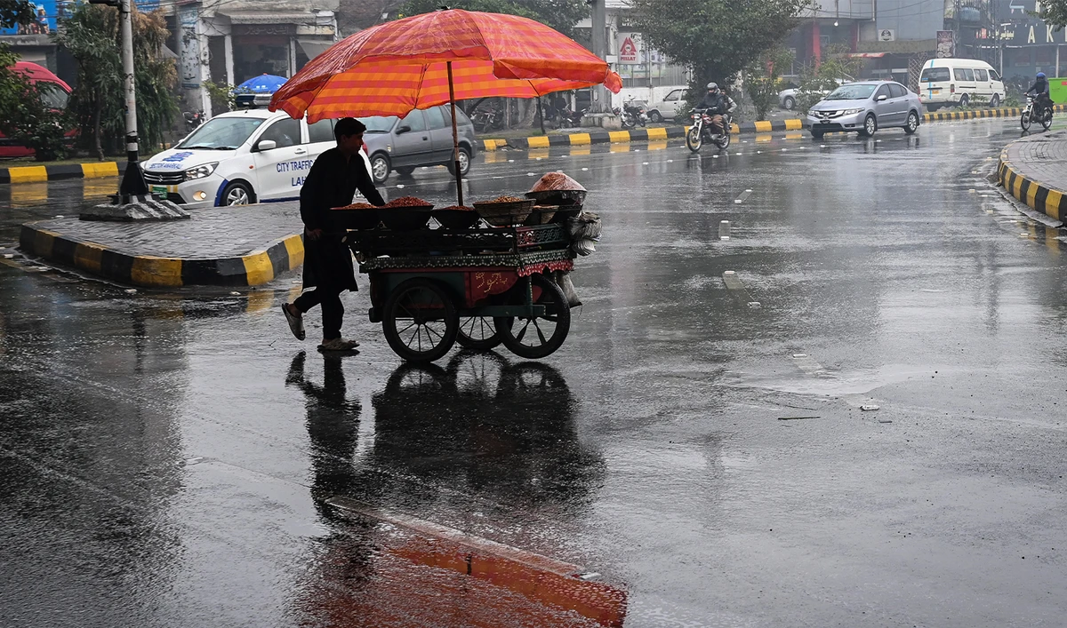 A vendor pushes his food cart as he walks across a road during rainfall in Lahore on December 27, 2024. (AFP/File)
