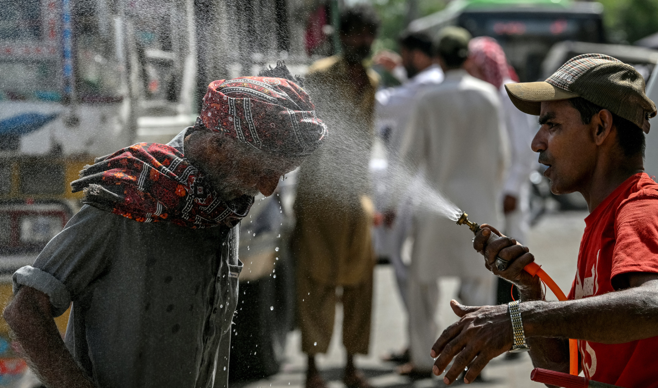A volunteer of the Edhi Foundation sprays water on a passerby's head to cool off on a hot summer day along a road amid the ongoing heatwave in Karachi on April 21, 2025. (AFP)