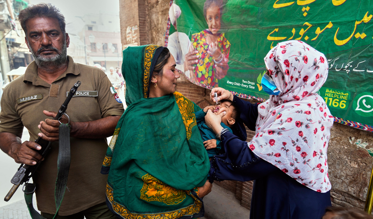 A police officer stands guard (left) as a health worker (right) administers a polio vaccine to a child at a neighborhood of Lahore, Pakistan, on April 21, 2025. (AP)