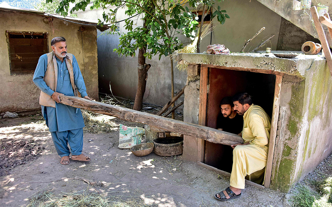 This photograph taken on April 28, 2025 shows Shabbir Awan (L) with his relatives clearing a wooden log from an underground bunker in the Chakothi village of Azad Kashmir, about 3kms from the Line of Control (LoC). (AFP)