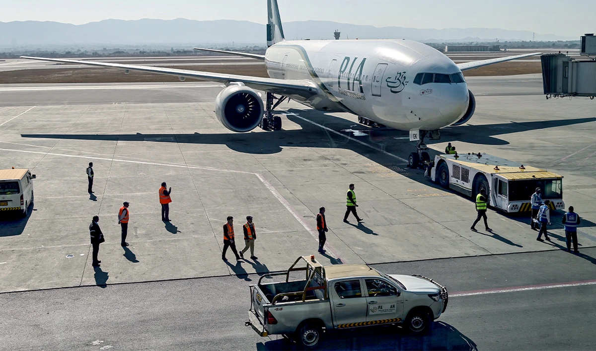 Ground staff stand next to the Pakistan International Airline (PIA) aircraft ahead of its takeoff for Paris at the Islamabad International Airport on January 10, 2025. (AFP/File)