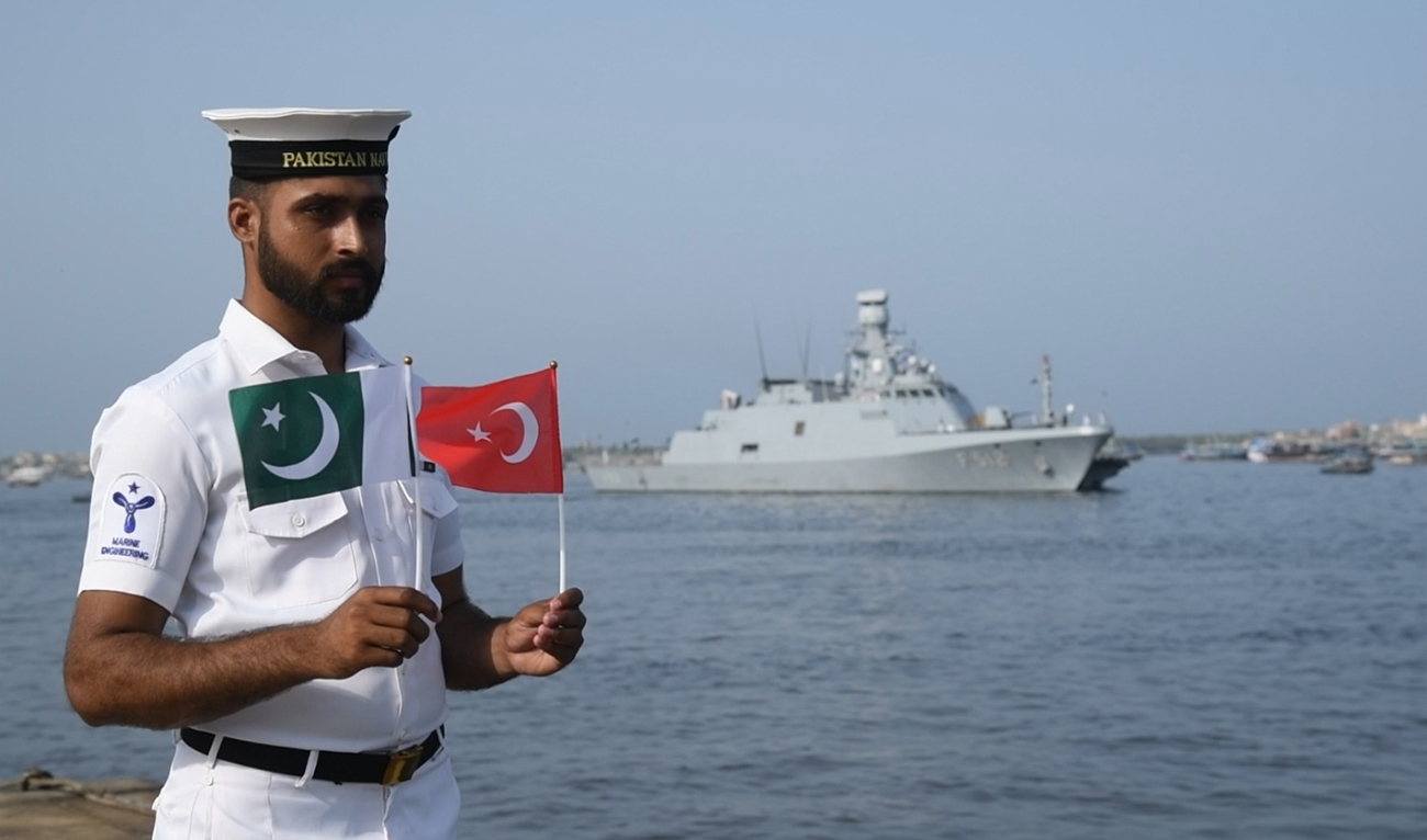In this handout photograph, taken and released by Director General Public Relations Pakistan Navy on May 3, 2025, Pakistan Navy official holds national flags of Pakistan and Turkiye as Turkish Navy Ship TCG BÜYÜKADA (F-512) arrived in Karachi. (Photo courtesy: Pakistan Navy)