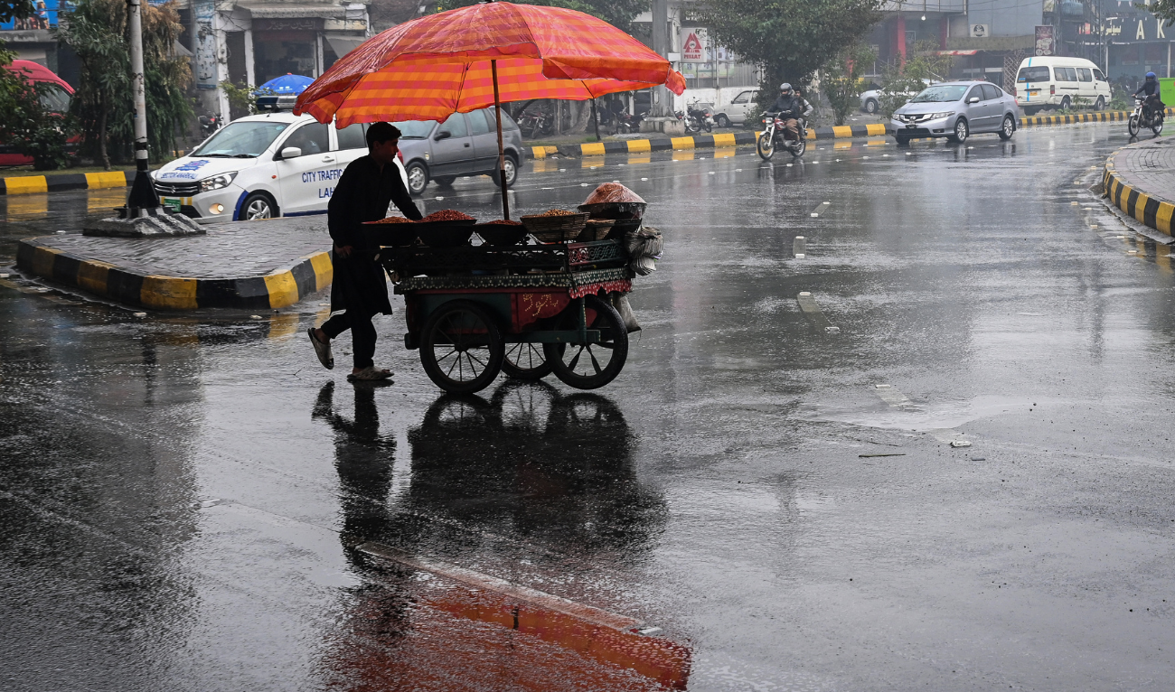 A vendor pushes his food cart as he walks across a road during rainfall in Lahore on December 27, 2024. (AFP)