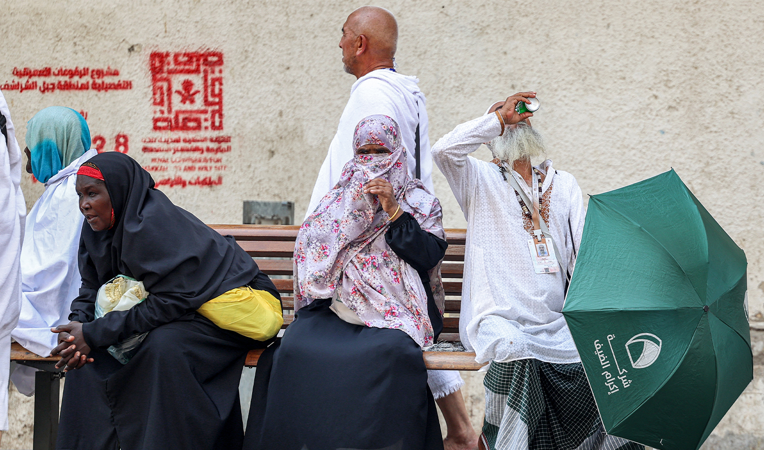 A departing Muslim pilgrim has a drink from a man as he sits next to other women in Saudi Arabia's holy city of Makkah on June 20, 2024. (AFP/File)