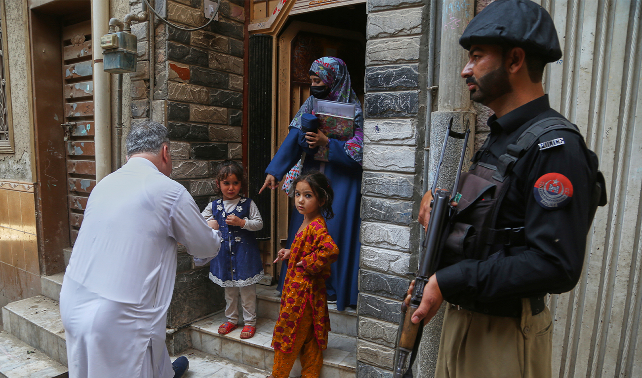 A police officer stands guard as a health worker (left) marks a finger of a child after administering a polio vaccine at a neighborhood in Peshawar, Pakistan, on May 26, 2025. (AP/File)