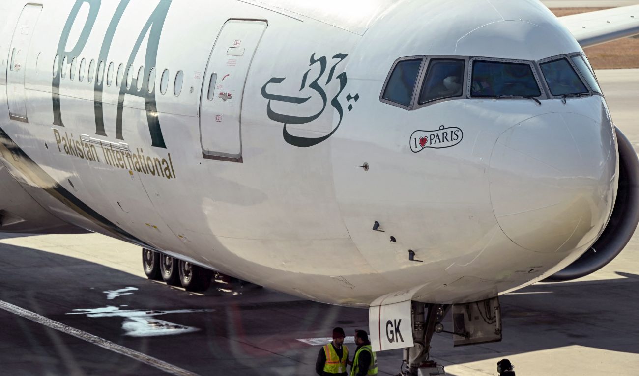 Ground staff stand next to the Pakistan International Airline (PIA) aircraft ahead of its takeoff for Paris at the Islamabad International Airport on January 10, 2025. (AFP/file)