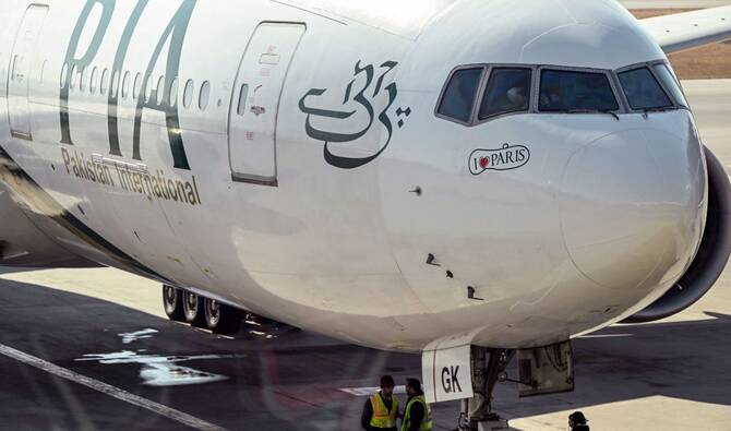 Ground staff stand next to the Pakistan International Airline (PIA) aircraft ahead of its takeoff for Paris at the Islamabad International Airport on January 10, 2025. (AFP/file)
