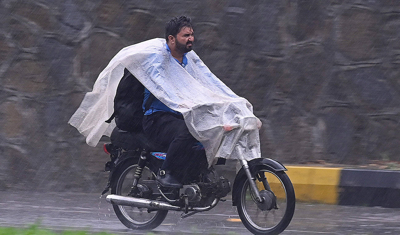 A motorist wearing a plastic sheet, makes his way along a road as it rains in Islamabad on June 26, 2025.(AFP)