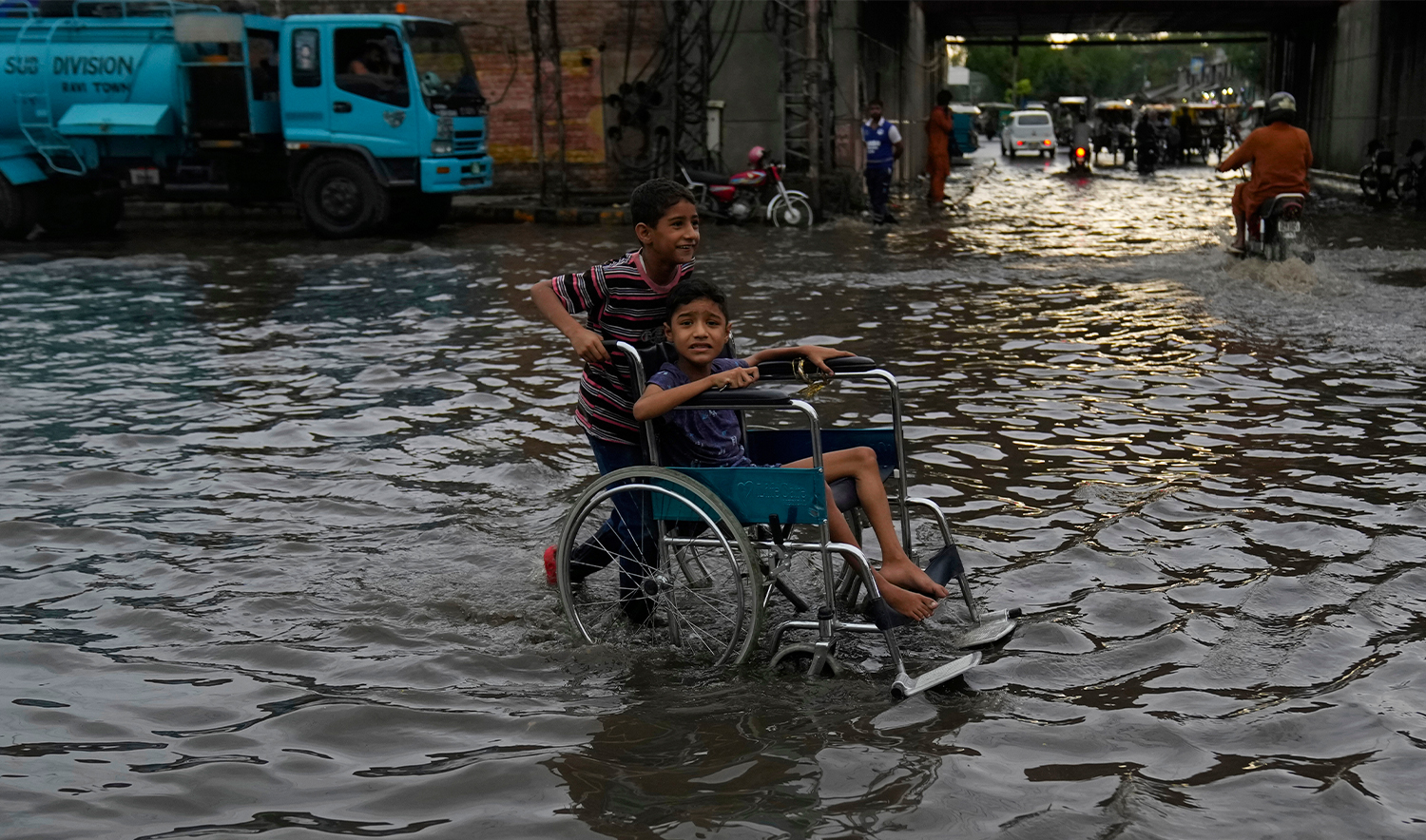 A boy pushes his cousin on wheelchair through a flooded road caused by heavy monsoon rains, in Lahore, Pakistan, on June 29, 2025. (AP)