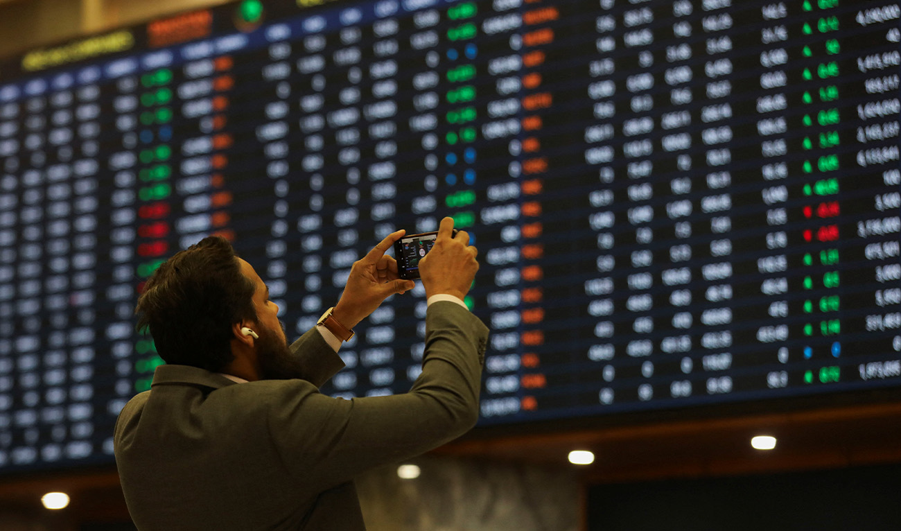 A man uses a mobile phone as he takes a photo of the electronic board displaying share prices during a trading session at the Pakistan Stock Exchange, in Karachi, Pakistan, on November 28, 2023. (Reuters/File)