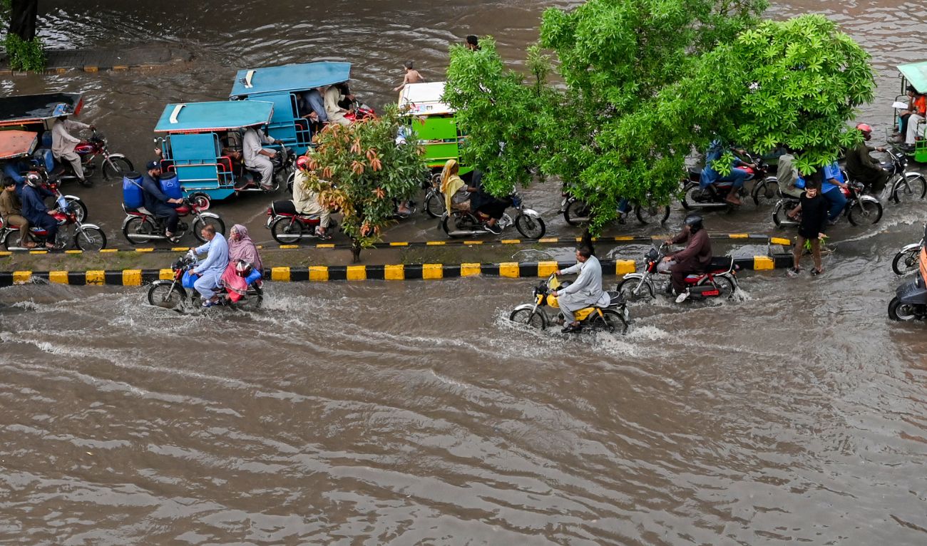 Commuters cross a flooded street after heavy monsoon rains in Lahore on July 9, 2025. (AFP)