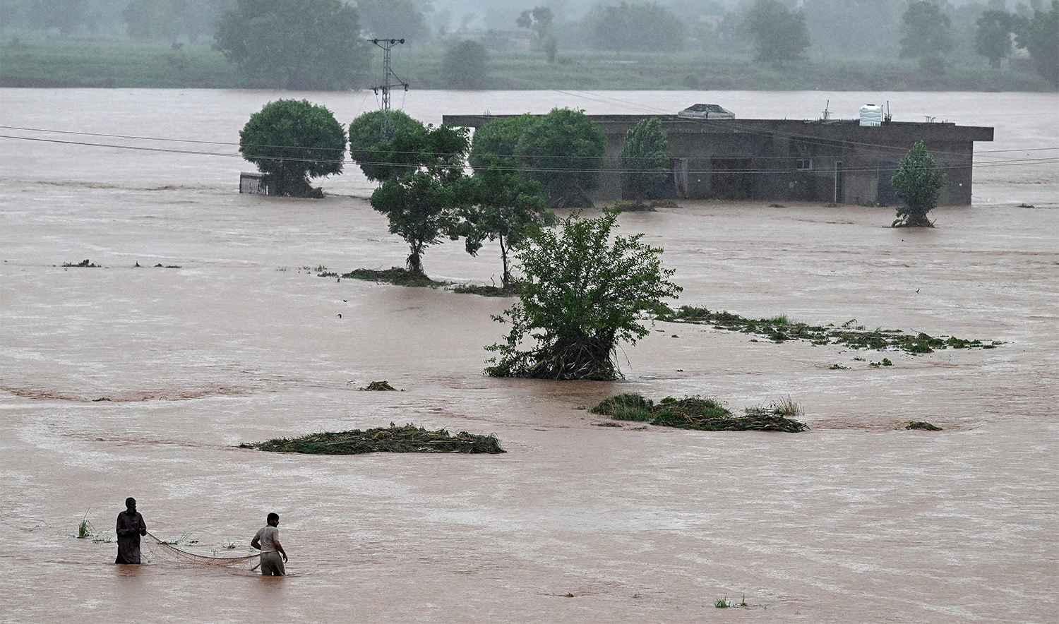 Local people catch fish in the floodwaters near a partially submerged house during heavy monsoon rains at the Ladian village of Rawalpindi on July 17, 2025. (AFP)