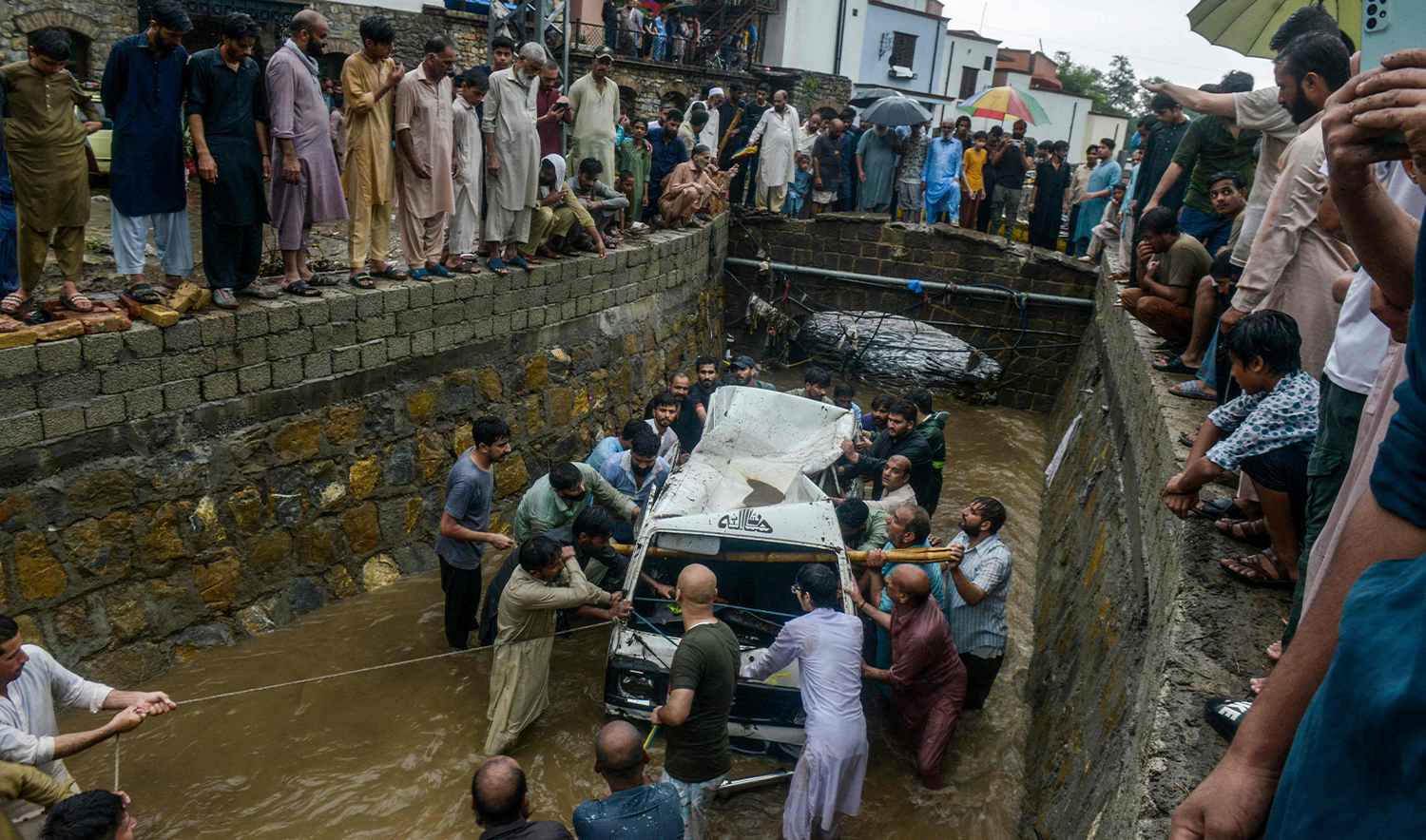People remove the wreckage of a van from a drainage after heavy monsoon rains in Islamabad on July 21, 2025. (AFP)