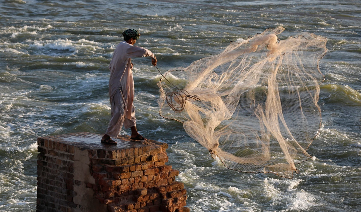A man casts a net to catch fish from the flow of flood waters in Sehwan, Pakistan on September 30, 2022. (REUTERS/File)