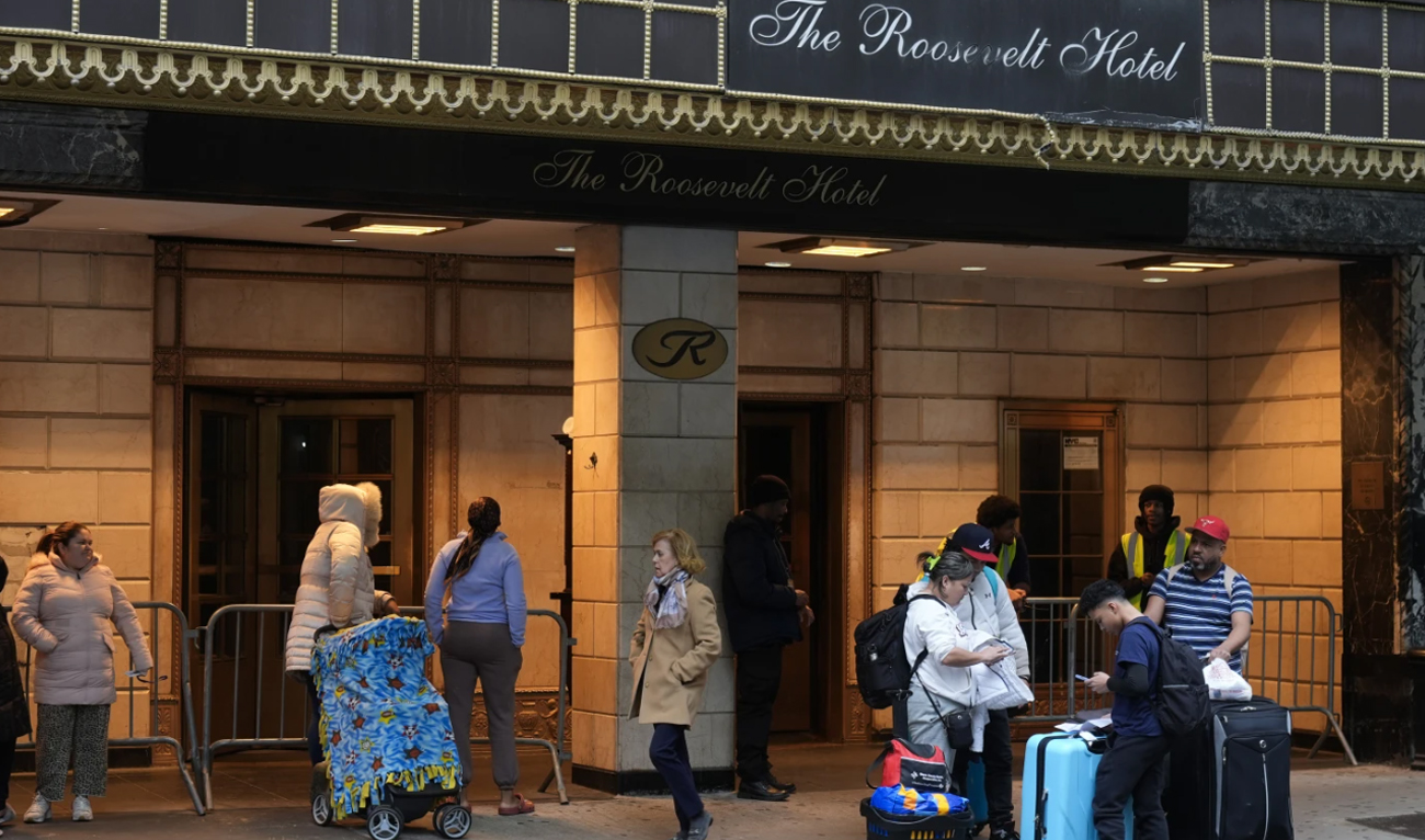 Migrants wait for a ride, with their belongings, in front of the Roosevelt Hotel in New York on February 25, 2025. (AP/File)