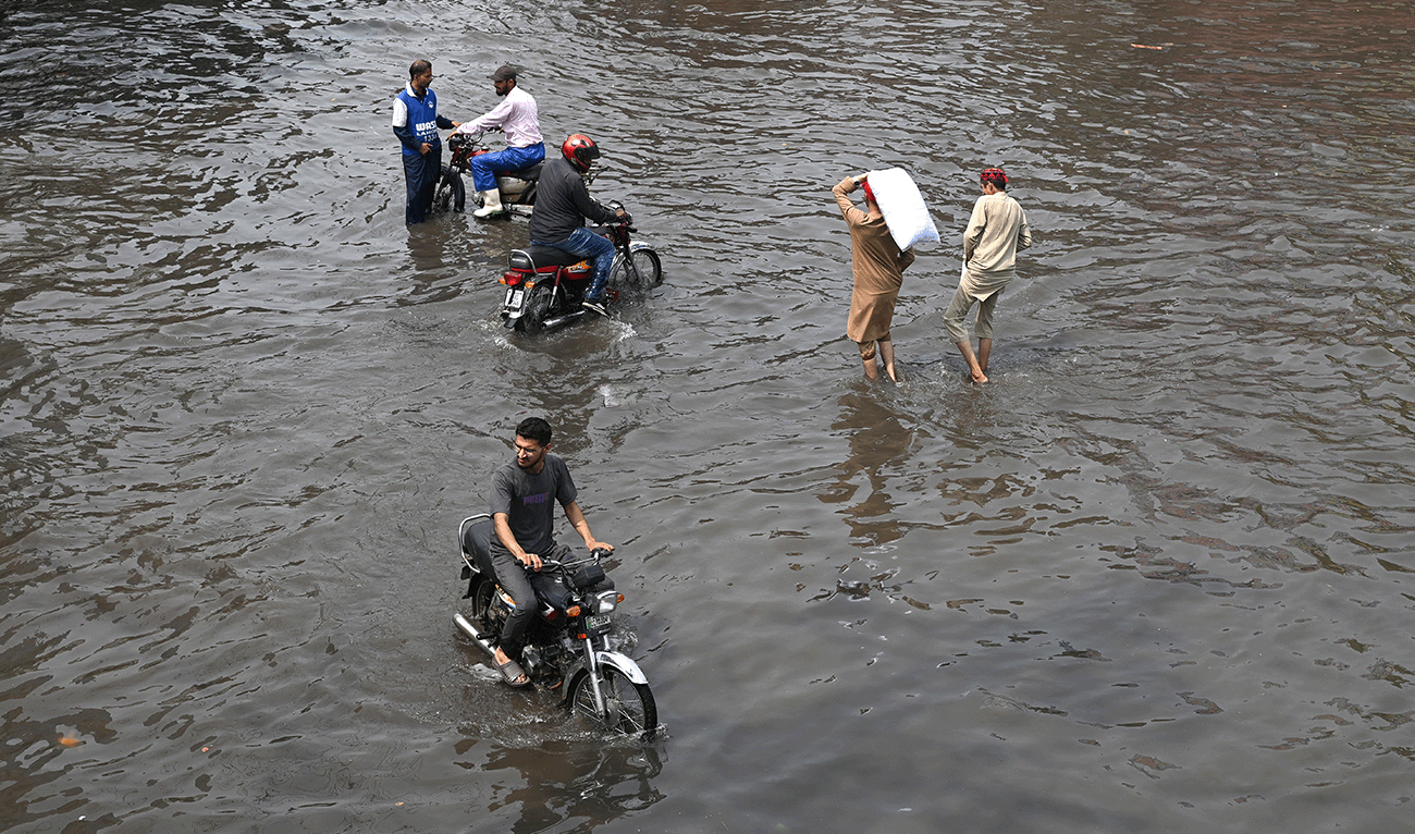 Commuters wade through a flooded street after heavy monsoon rains in Lahore on August 3, 2025. (AFP/File)