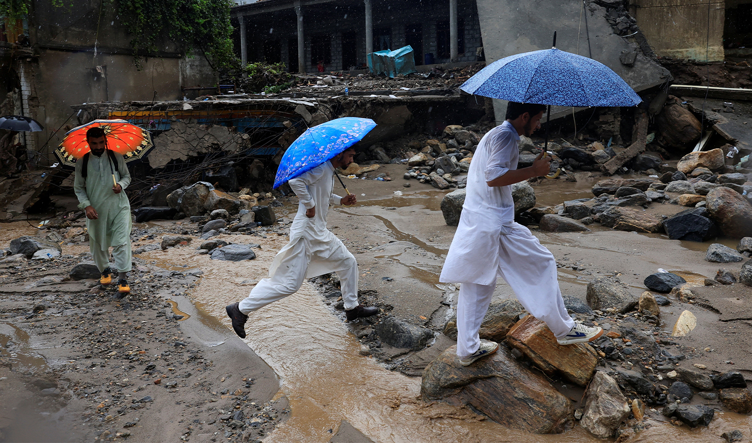 Volunteers walks with umbrellas to avoid rain as they survey the damaged areas, following a storm that caused heavy rains and flooding in Bayshonai Kalay, in Buner district, in Khyber Pakhtunkhwa province, Pakistan, on August 18, 2025. (REUTERS)