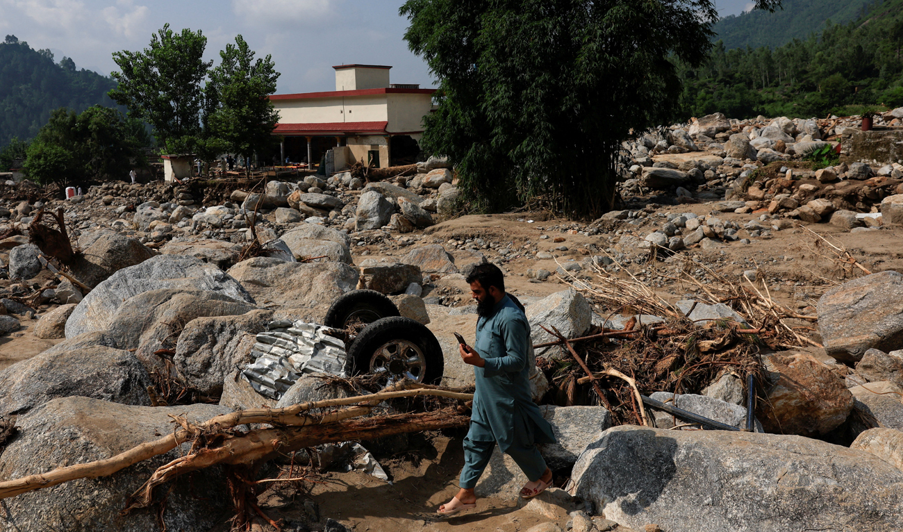 A resident walks past the remains of a vehicle stucked amid rocks and boulders, following a storm that caused heavy rains and flooding in Qadir Nagar area, in Buner district, Khyber Pakhtunkhwa province, Pakistan on August 21 2025. (REUTERS)