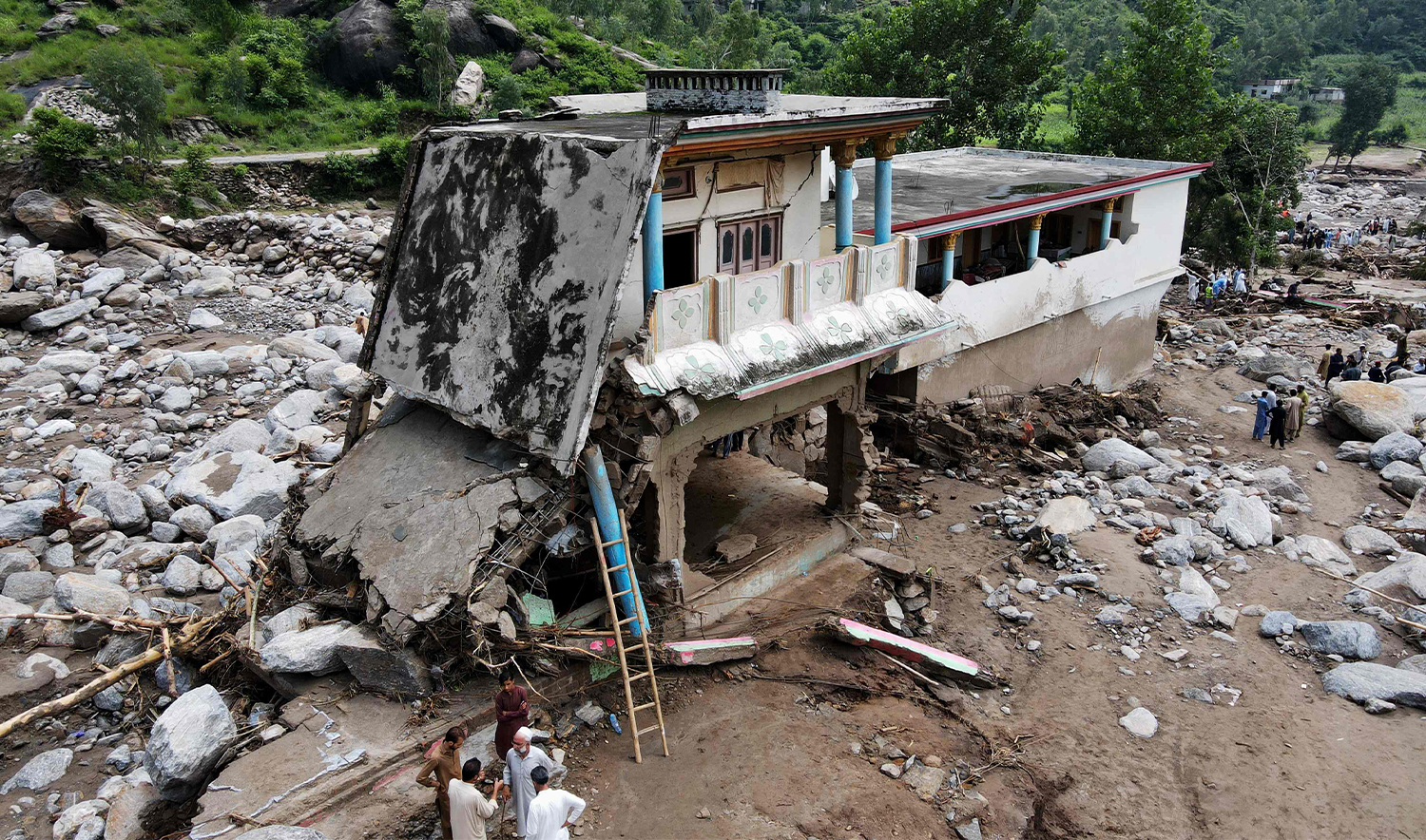 An aerial view shows flood survivors standing near a damaged house surrounded by heavy rocks in the Buner district of mountainous Khyber Pakhtunkhwa province on August 17, 2025. (AFP)