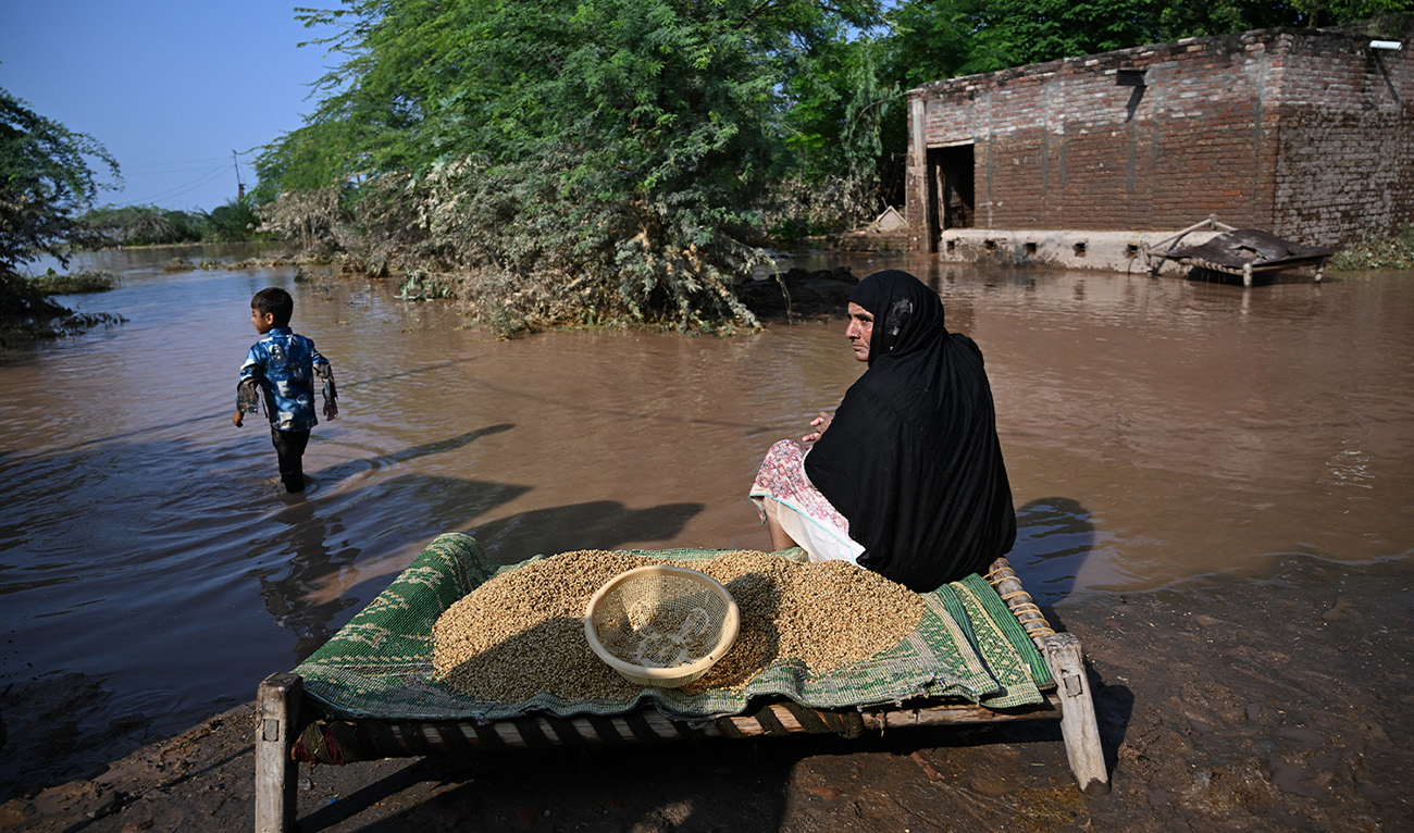 A woman sits next to wheat amidst floodwaters at Chak Ali Sher village in Wazirabad district on August 28, 2025, after the government issued a flood alert for riverside areas of Punjab province. (AFP/File)