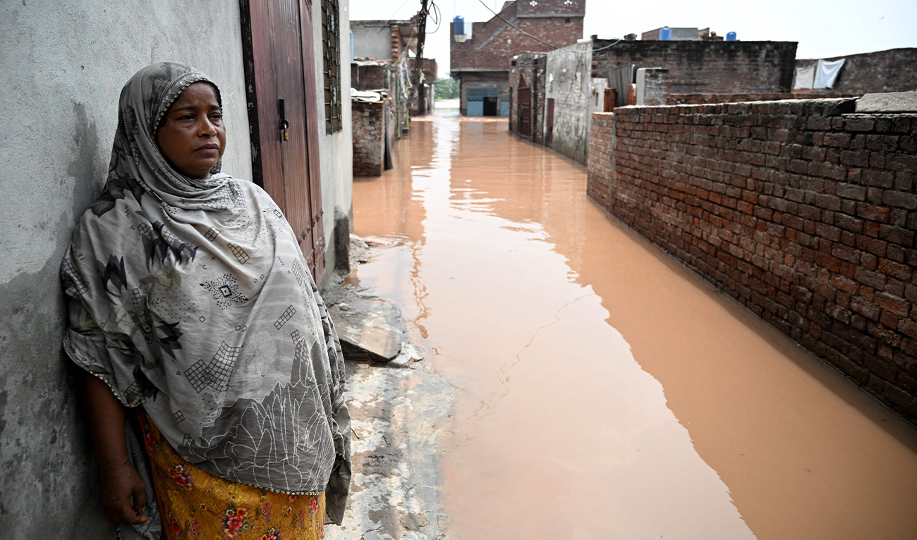 A woman stands near her submerged home, after floodwaters entered from the overflowing Ravi river in Shahdara, Lahore on August 29, 2025. (FP)