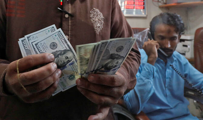 An employee of a foreign exchange shop counts U.S. dollar banknotes from behind a glass booth in Karachi, Pakistan, on September 7, 2023. (REUTERS/File)