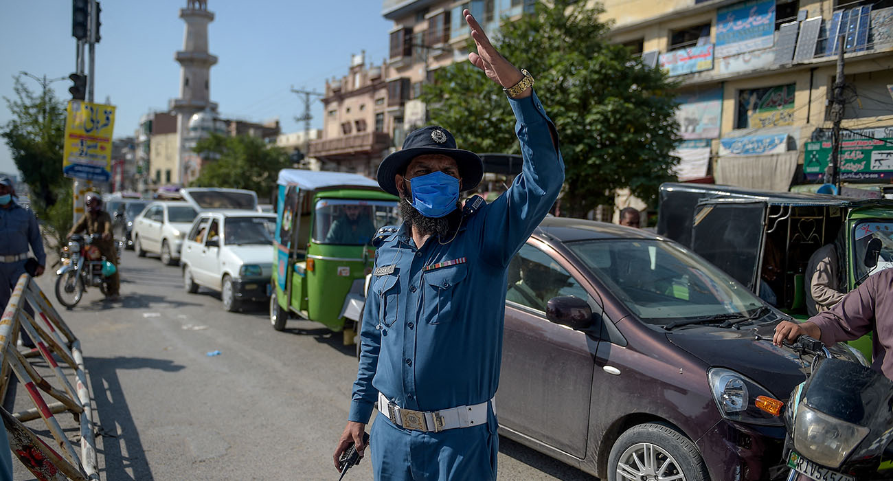 In this picture taken on July 22, 2020, a traffic policeman (C) wearing a facemask as a preventive measure against the COVID-19 coronavirus gestures to motorists along a road outside the Raja Bazar in Rawalpindi. (AFP/ file)