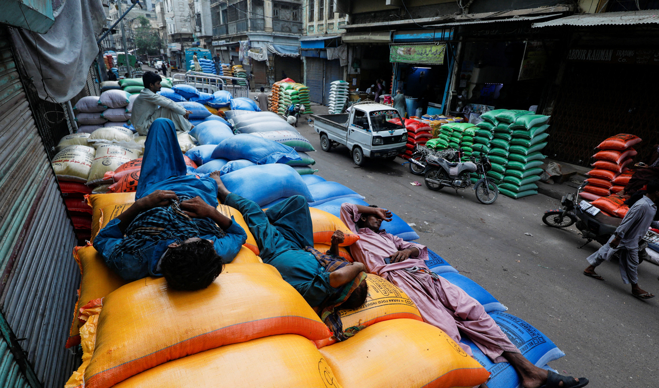 Laborers take nap on the sacks of grains and sugar, after offloading from a supply truck, outside shops at the wholesale grain market in Karachi, Pakistan on July 20, 2023. (REUTERS/File)