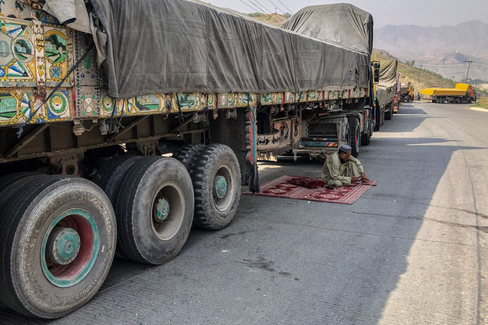 A truck driver rests beside his stalled vehicle along a road near the closed Pakistan-Afghanistan border town of Torkham on October 19, 2025. (AFP)