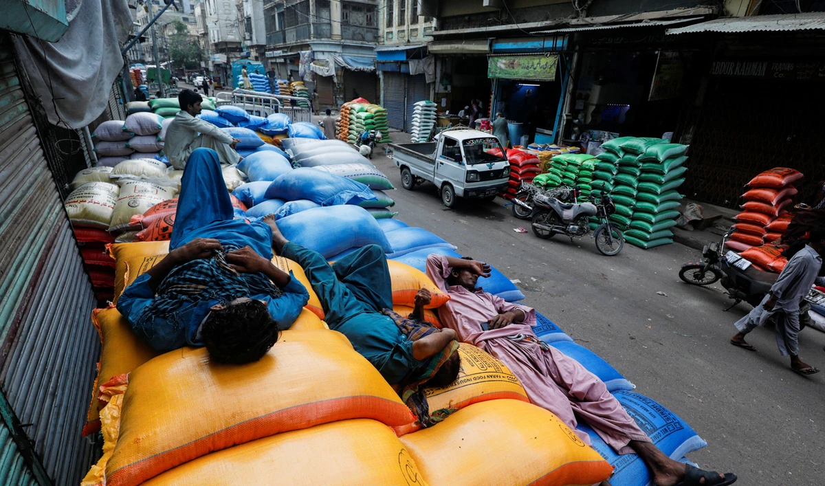Laborers take nap on the sacks of grains and sugar, after offloading from a supply truck, outside shops at the wholesale grain market in Karachi, Pakistan on July 20, 2023. (REUTERS/File)