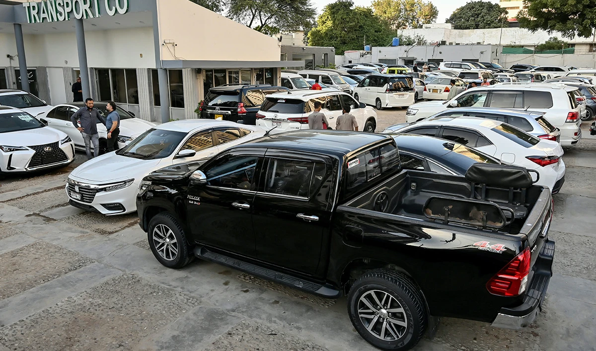 This photograph taken on November 11, 2024 shows car dealer Fahad Nazir (2L) speaking to a customer near a Toyota Hilux pick-up truck (front) locally known as 'Dala', parked at his showroom yard in Karachi. (AFP)