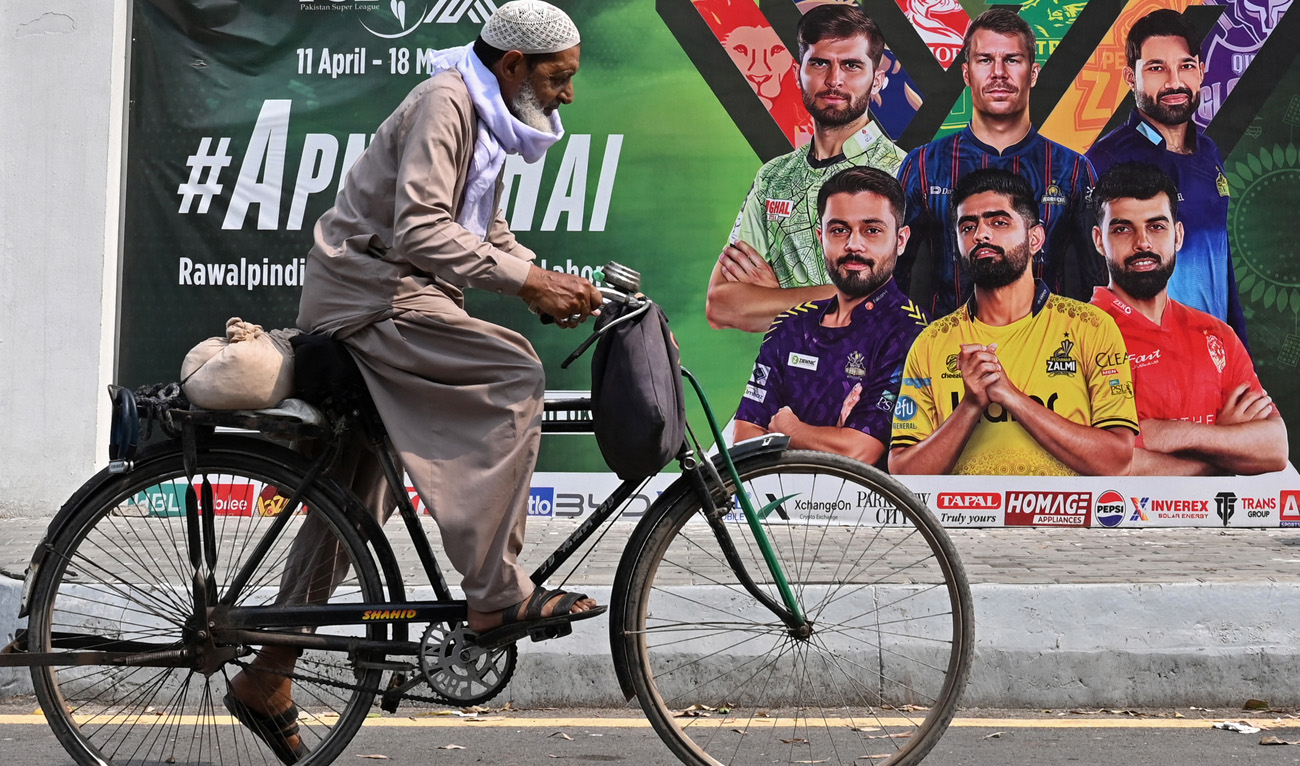A cyclist rides past a hoarding outside the Gaddafi Cricket Stadium, one of the venues for the Pakistan Super League (PSL), in Lahore on May 9, 2025. (AFP/File)