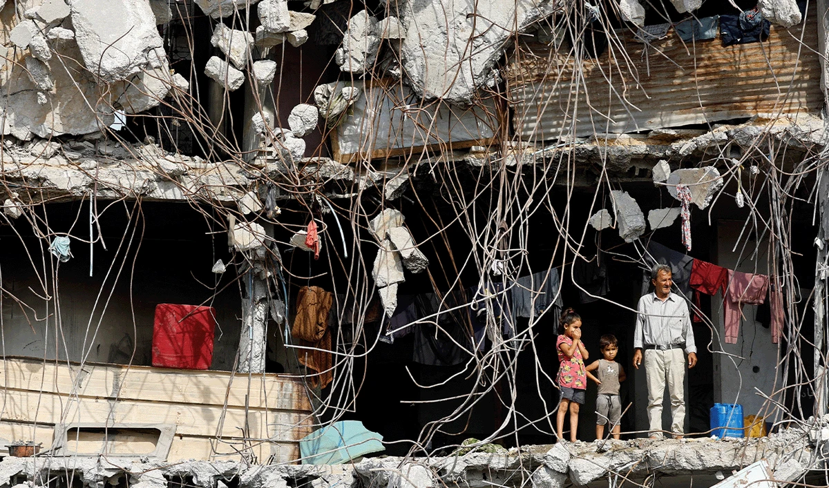 A Palestinian man and children stand at a heavily damaged building surrounded by exposed rebar and rubble, in Gaza City, November 2, 2025. (Reuters/File)