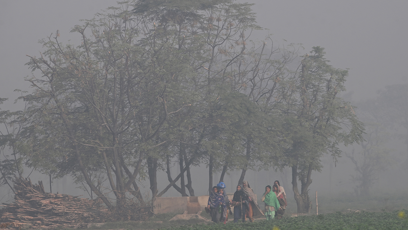 Women walk through a field amid smoggy conditions on the outskirts of Lahore, Pakistan, on November 24, 2025. (AFP/File)