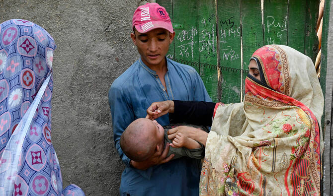 The photograph taken on October 5, 2024, shows a health worker (R) administering polio drops to a child during a door-to-door poliovirus vaccination campaign on the outskirts of Peshawar, Pakistan. (AFP/File)
