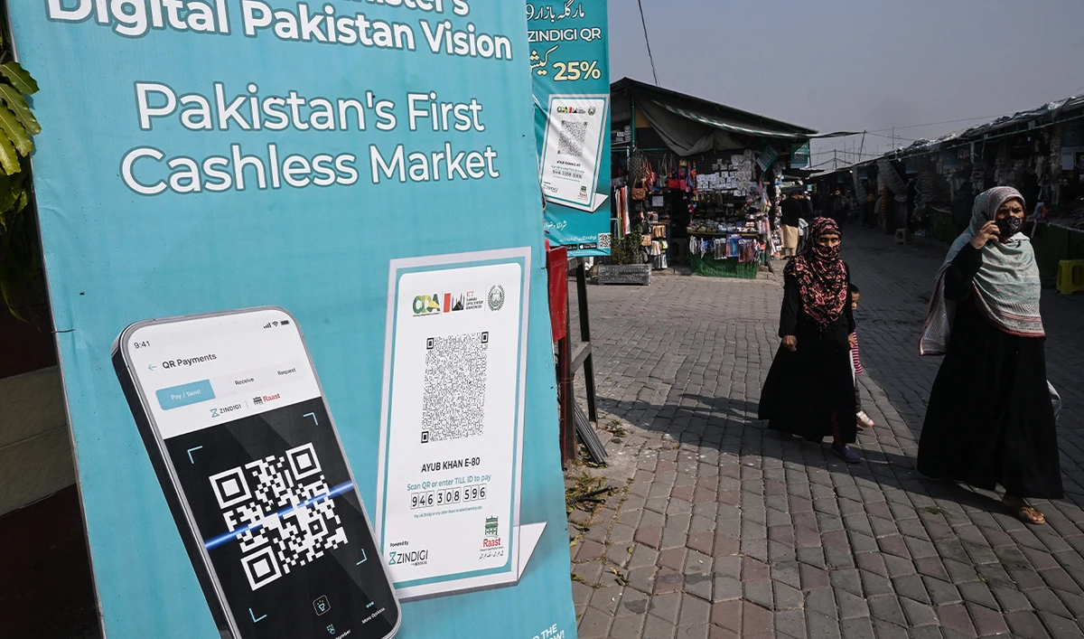 Women walk past an advertisement promoting digital cashless payment using QR (quick response) codes at a market in Islamabad on November 25, 2025. (AFP/File)