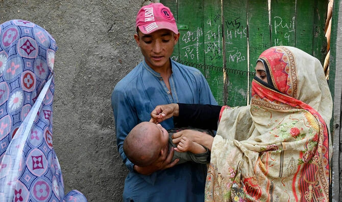 The photograph taken on October 5, 2024, shows a health worker (R) administering polio drops to a child during a door-to-door poliovirus vaccination campaign on the outskirts of Peshawar, Pakistan. (AFP/File)