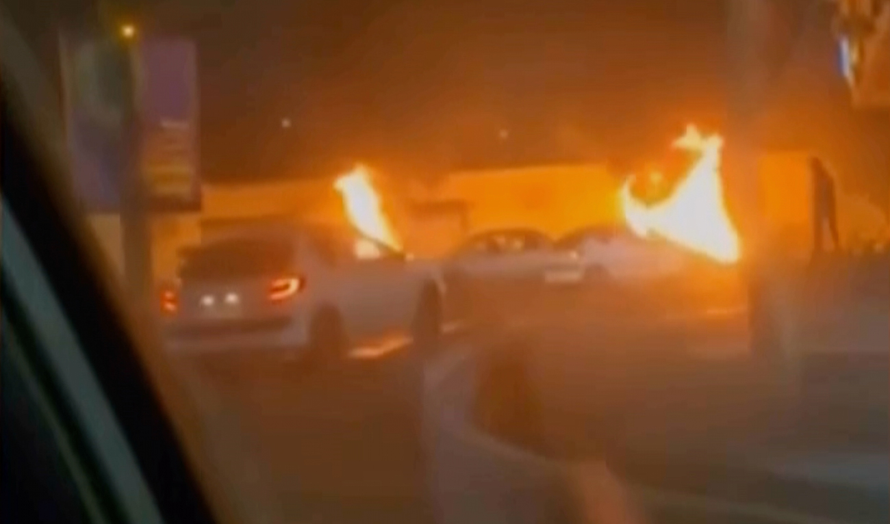 The screengrab taken from a video released by Iranian state television on January 9, 2026, shows cars driving past burning vehicles during a night of mass protests in Tehran, Iran. (Iranian State TV/AP)