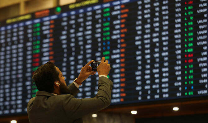 A man uses a mobile phone as he takes a photo of the electronic board displaying share prices during a trading session at the Pakistan Stock Exchange, in Karachi, Pakistan on November 28, 2023. (REUTERS/File)