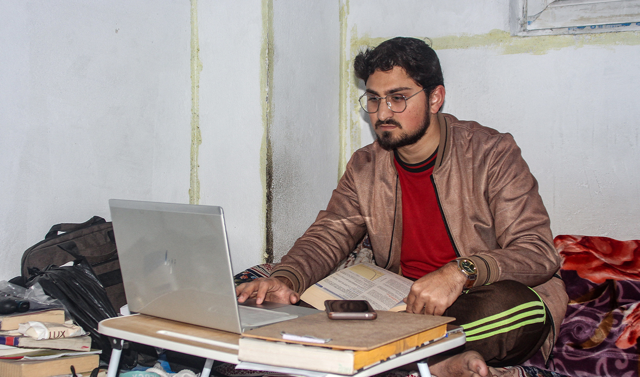 This photograph taken on December 29, 2025 shows Shah Faisal, a Pakistani national studying at an Afghan university, using his laptop at his residence in Jalalabad. (AFP)