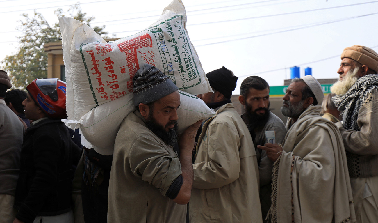 A man carries sacks of flour on his shoulder, while others stand in queue to purchase from a truck along a road in Peshawar, Pakistan January 20, 2020. (Reuters/File)